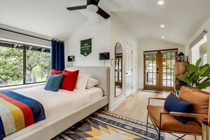 A modern bedroom with a large bed, a ceiling fan, a view of the outdoors, and a green sign on the wall.