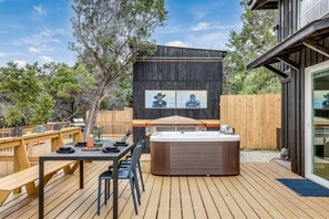 A wooden deck with a hot tub, a table with chairs, and a wooden fence.