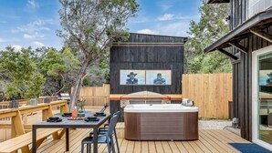 Una terraza de madera con un jacuzzi, una mesa y sillas, y una valla de madera.