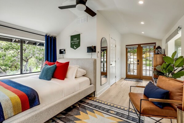 A modern bedroom with a large bed, a ceiling fan, a view of the outdoors, and a green sign on the wall.