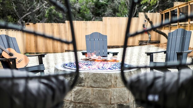 Eine Terrasse mit Feuerstelle, zwei Adirondack-Stühlen und einer Gitarre.