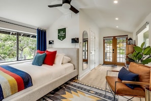 A modern bedroom with a large bed, a ceiling fan, a view of the outdoors, and a green sign on the wall.