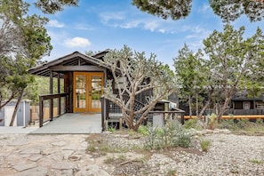 A rustic cabin with a wooden porch, a front door, and a staircase leading to a deck.