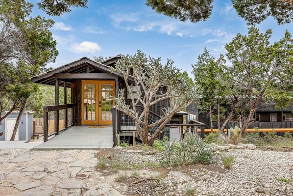 A rustic cabin with a wooden porch, a front door, and a staircase leading to a deck.