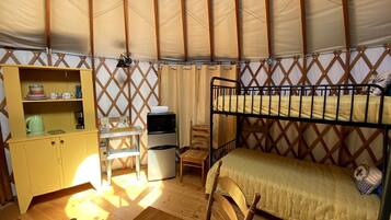 A compact room with a bunk bed, a small desk with a chair, a kitchenette, and a storage cabinet.
