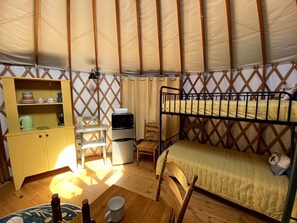 Une chambre compacte comprenant un lit superposé, un petit bureau avec une chaise, une kitchenette et un placard de rangement.