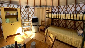 A compact room with a bunk bed, a small desk with a chair, a kitchenette, and a storage cabinet. - Beautiful Upstate New York Luxury Camping Yurt on a Farm (Granville)