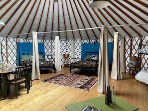 A yurt with two beds, a dining area, and a wooden floor.