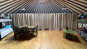 A yurt with a wooden floor, a dining table with chairs, a sofa, and a small table with bottles. - Gorgeous Yurt for Family Getaways in Upstate New York (Granville)