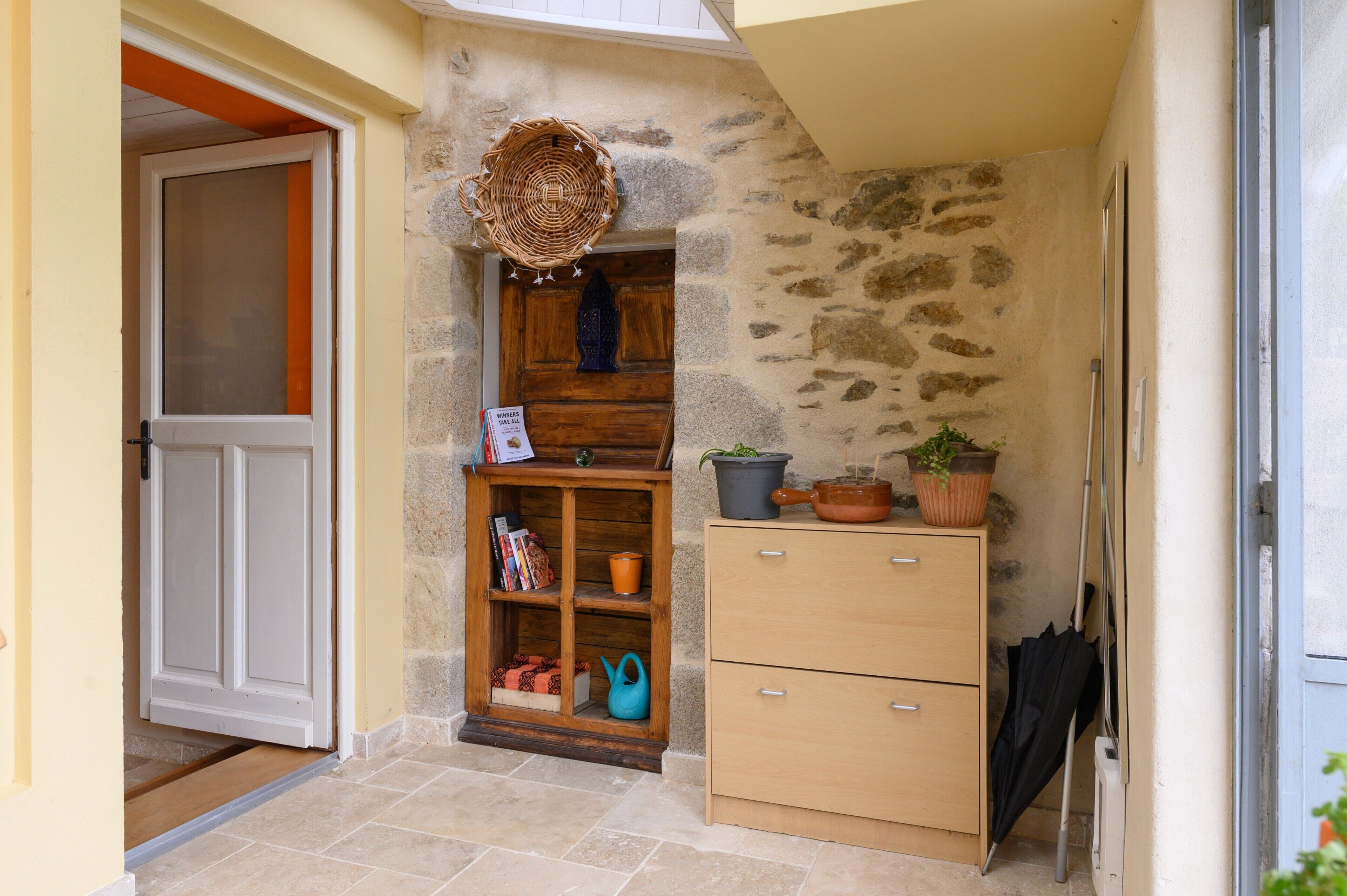 A stone wall, wooden door, wicker basket, potted plants, and a wooden cabinet.