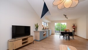 Un salon moderne doté d’un téléviseur à écran plat, d’un meuble de rangement en bois et d’un coin repas avec une table et des chaises.