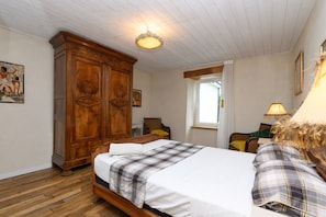 Un dormitorio con un armario de madera, una cama con edredón escocés, una ventana con vistas y una lámpara en una mesita de noche.