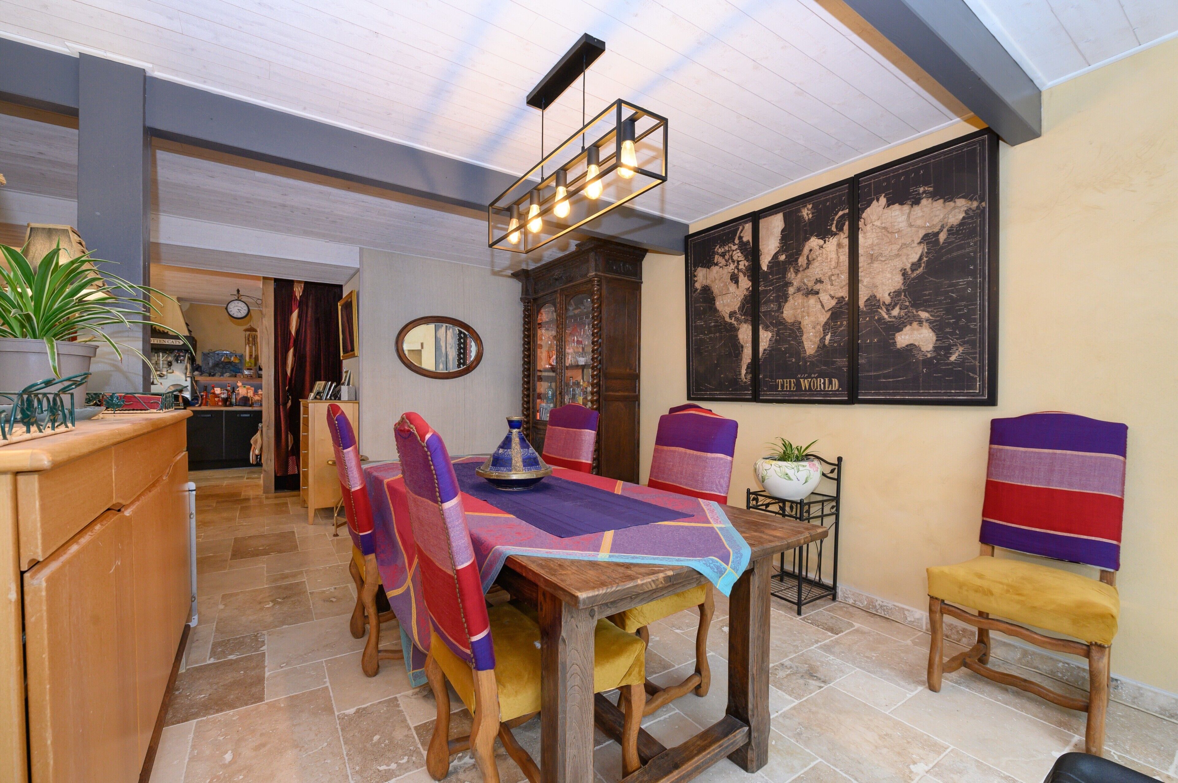 A dining area with a wooden table, chairs, a world map on the wall, and a hanging light fixture.