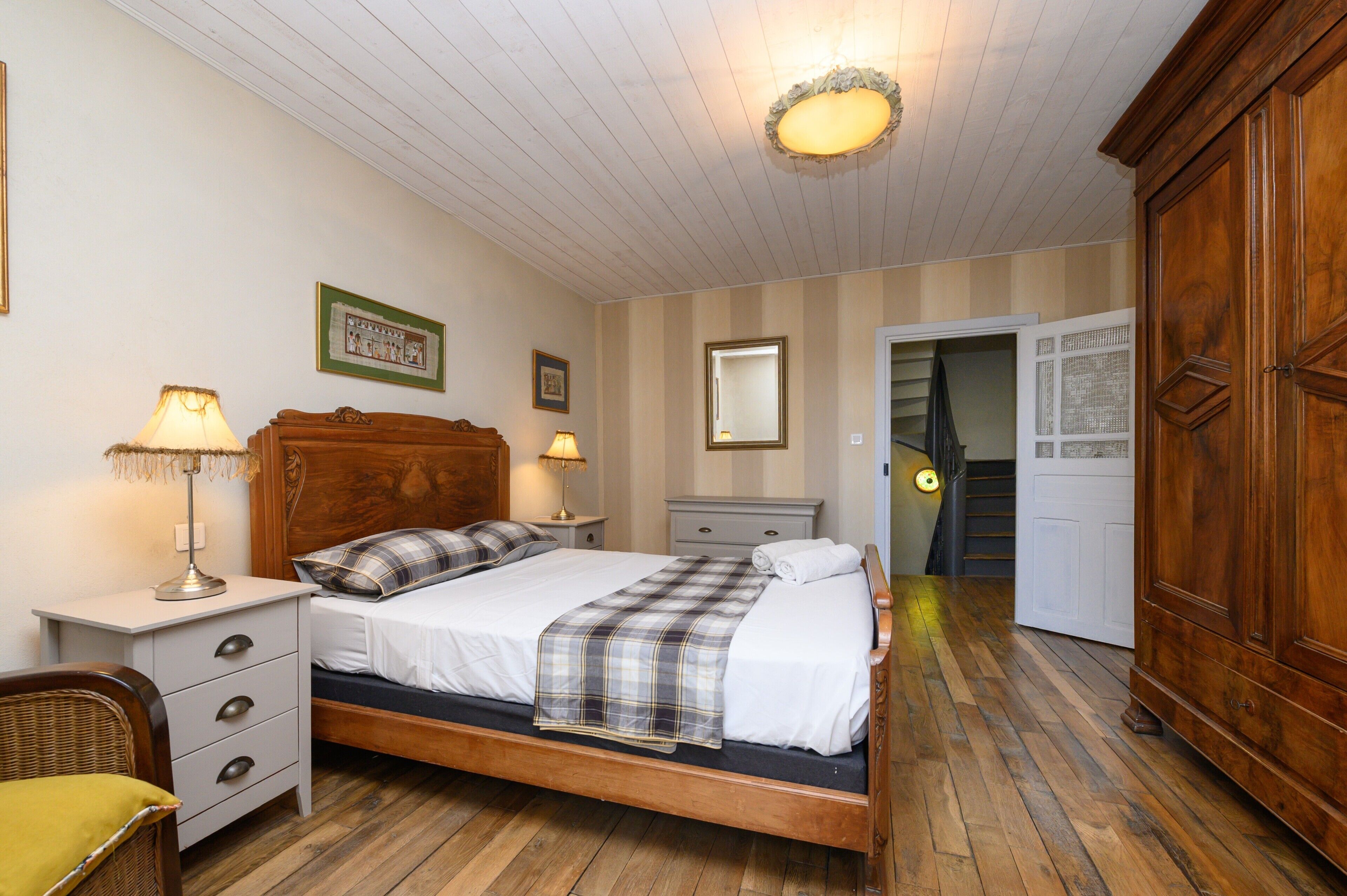 Un dormitorio con cama de madera, mesitas de noche, un armario y una escalera que lleva a otra habitación.