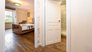 Un dormitorio con suelo de madera, una cama con manta escocesa, una mesita de noche con lámpara y una ventana con vistas.