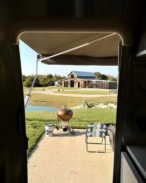 Vista desde el interior de un vehículo a un patio al aire libre con una parrilla, una mesa y una silla.