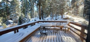 Eine Holzterrasse mit schneebedecktem Boden, umgeben von schneebehangenen Bäumen und Sitzmöbeln im Freien.