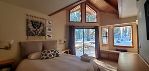 Ein Schlafzimmer mit einem großen Bett, Blick auf ein verschneites Deck und einer hohen Decke mit Holzbalken.