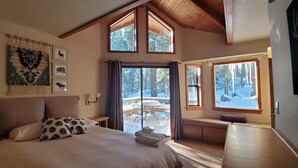 Un dormitorio con una cama grande, vistas a una terraza nevada y un techo alto con vigas de madera.