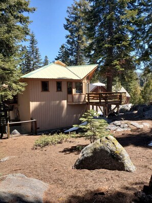 Une cabane en bois dotée d’une terrasse, entourée d’arbres et de rochers.
