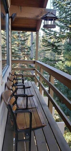 A wooden deck with a row of chairs, a lantern, and a view of a forest.