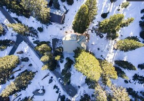 Vista aérea de una zona residencial con una casa rodeada de árboles cubiertos de nieve y un cielo despejado.