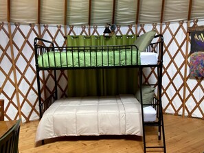 A bunk bed with a green curtain and a white mattress in a room with wooden flooring and a lattice wall. - Colorful Upstate New York Yurt Rental on a Farm (Granville)