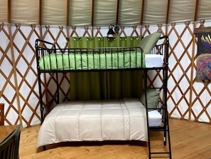 A bunk bed with a green curtain and a white mattress in a room with wooden flooring and a lattice wall. - Colorful Upstate New York Yurt Rental on a Farm (Granville)