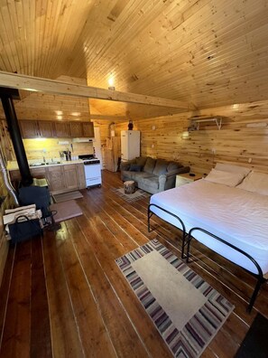 A cozy cabin interior with a wooden floor, a bed, a sofa, and a kitchenette area. - Schinzel Flats Hideaway near Pagosa Springs, CO (La Jara)