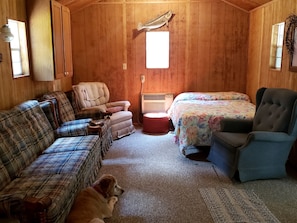 A cozy cabin interior with a plaid sofa, a chair, a bed with floral bedding, and a dog. - Private Pet-Friendly Cabins with Fire Pit for Nature Escapes in Clear Spring, Maryland, for Memorable Family Glamping Trips (Clear Spring)