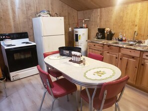 A kitchen with a stove, refrigerator, water heater, and a dining table with chairs.