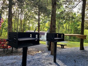 Un barbecue, une table de pique-nique et un banc situés dans une zone boisée.