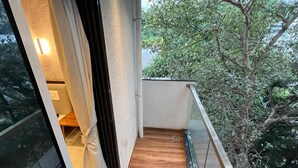 A narrow balcony with a wooden floor, glass railings, and a view of trees. - Hotel Sai Residency (Pune)