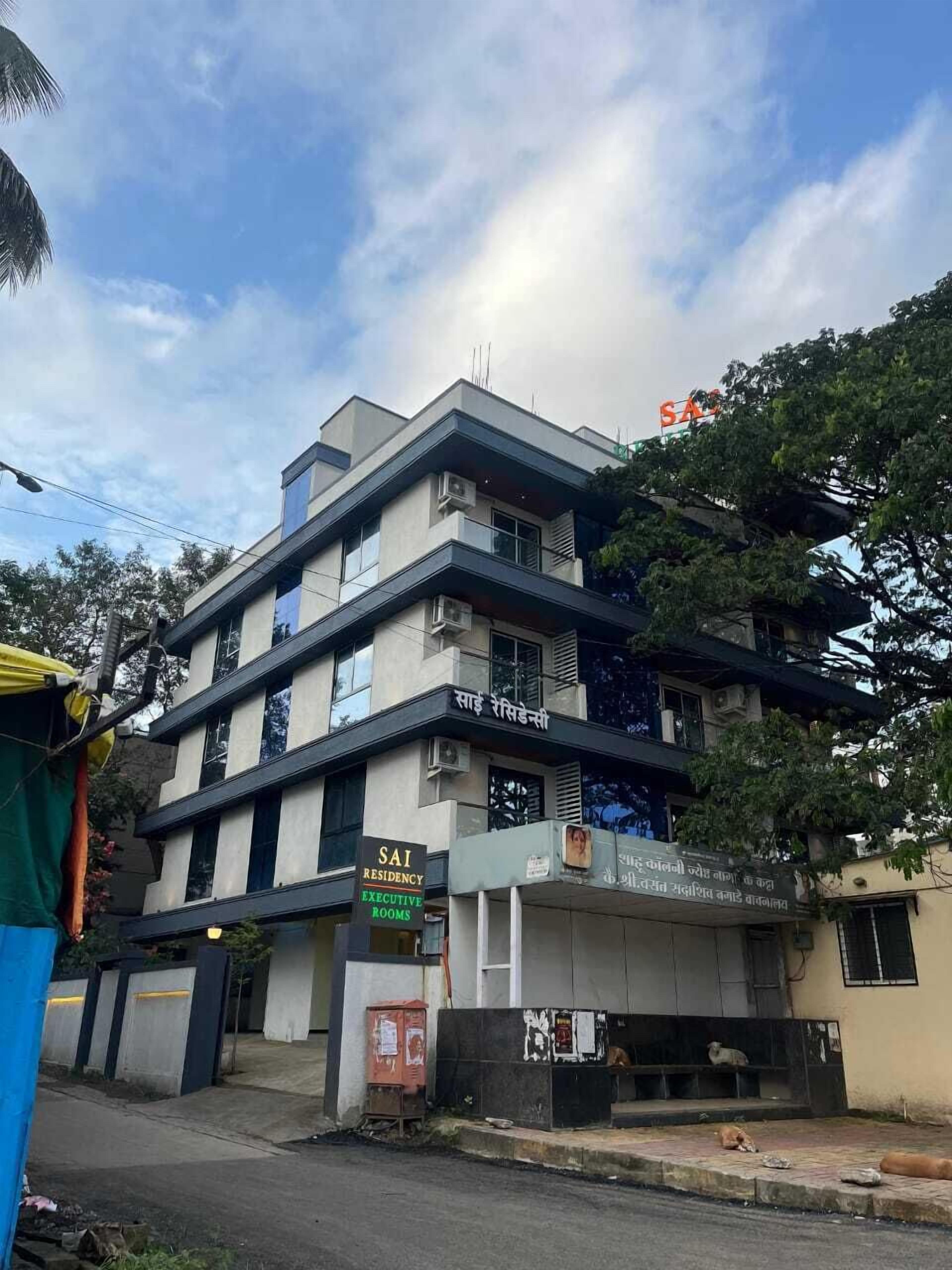 Un edificio de varios pisos con señalización que indica “SAI RESIDENCY EXECUTIVE ROOMS” y un letrero en un idioma local.