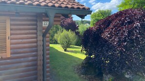 Una cabaña de madera con techo de tejas, un cartel con el número 22, y un jardín bien cuidado con arbustos y árboles variados.