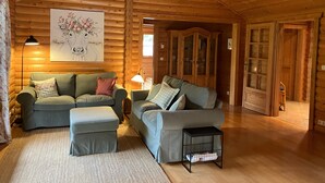 Interior de una cabaña de troncos con dos sofás, una lámpara, un armario y un cuadro.
