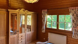 Una habitación de madera con cama, armario y ventana con cortinas.