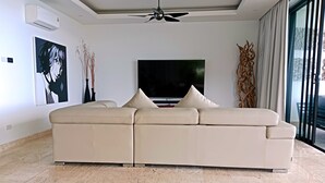 A modern living room with a beige sectional sofa, a flat-screen TV, and a ceiling fan. - Astoria Villa #2 – 3 Bed Pool Villa in Koh Samui (Chang Wat Surat Thani)