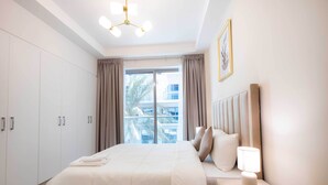 Habitación de hotel con una cama grande, una mesita de noche con lámpara, un armario y una ventana con cortinas.
