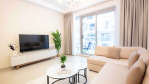Una sala de estar moderna con un televisor de pantalla plana, un sofá, una mesita de centro y un ventanal con cortinas.