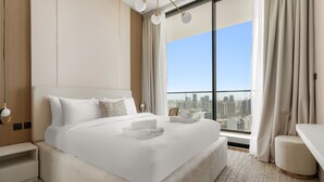 A modern hotel room with a large bed, a city view, and a small desk. - Binghatti Onyx - 3112 2BD (Dubai)