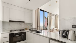 A modern kitchen with white cabinets, a built-in oven, a washing machine, and a large window with curtains. - Binghatti Onyx - 3112 2BD (Dubai)