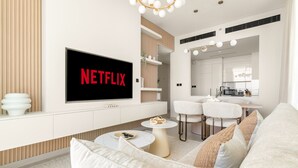 A modern living room with a flat-screen TV displaying "NETFLIX," a white sofa, a coffee table, and a dining area with chairs and a small table. - Binghatti Onyx - 3112 2BD (Dubai)