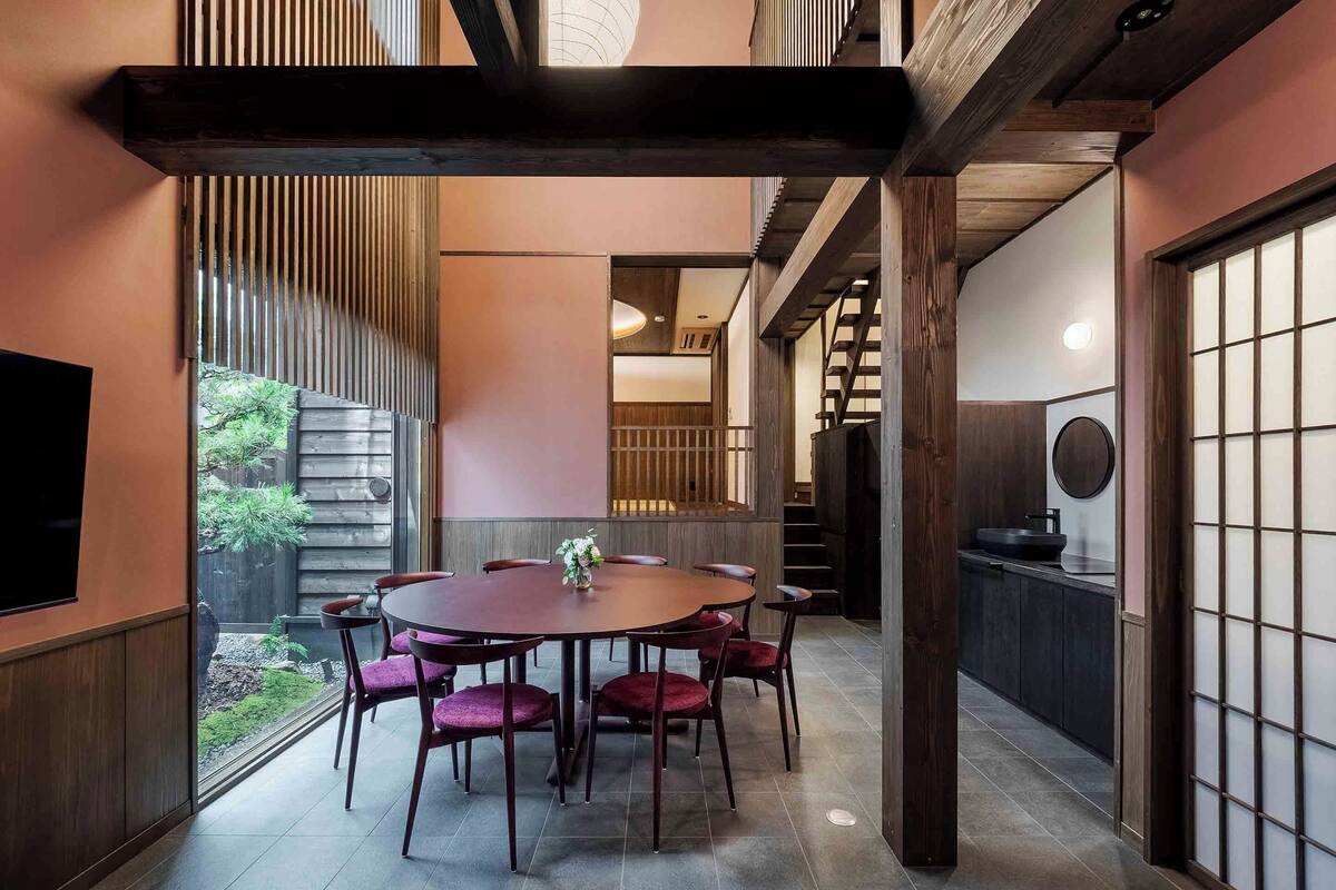 Un comedor tradicional japonés con una mesa redonda y sillas, vigas de madera y vistas a un jardín.