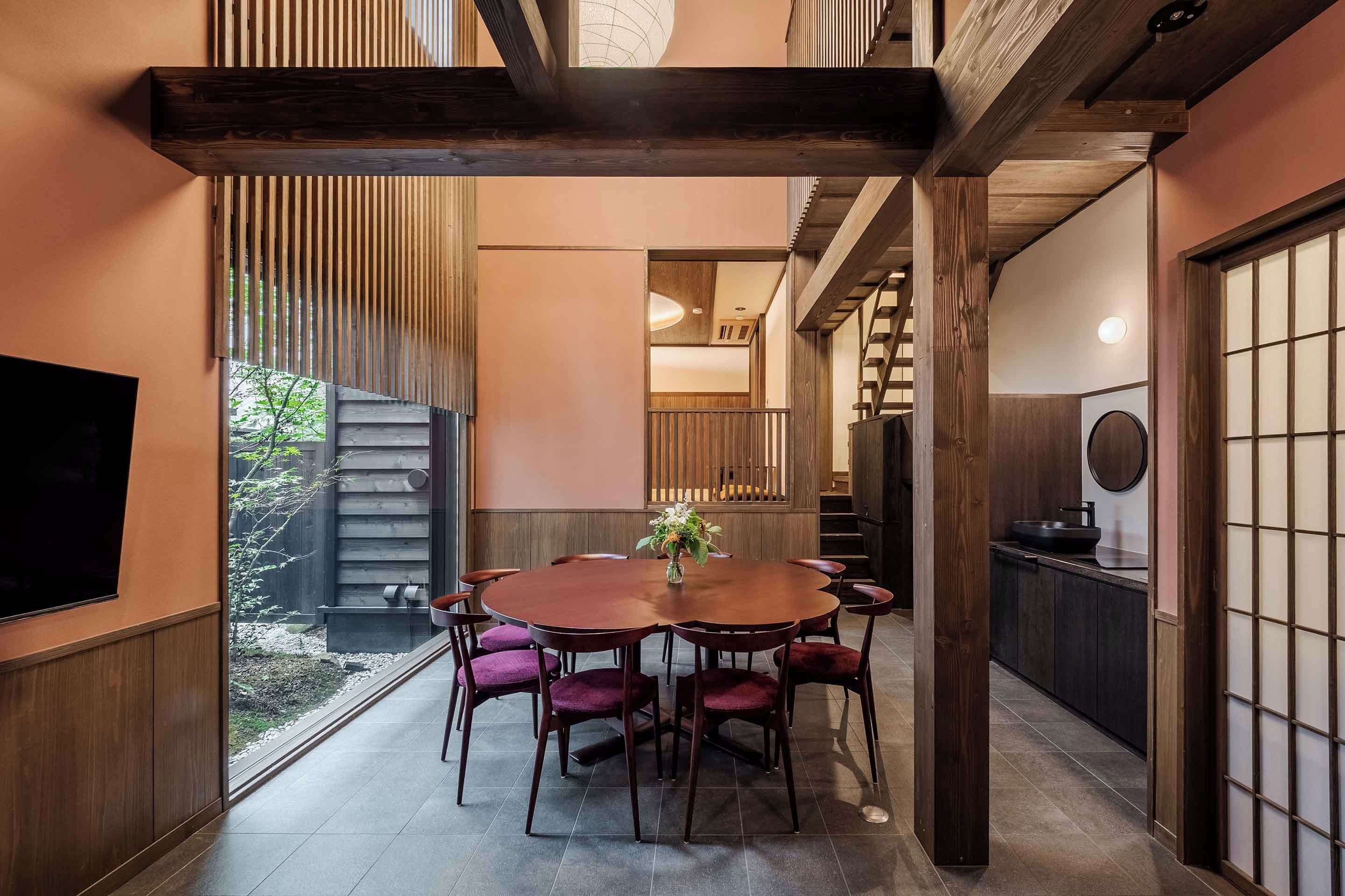 A dining area with a round table and chairs, a TV mounted on the wall, and a view of the outdoors.