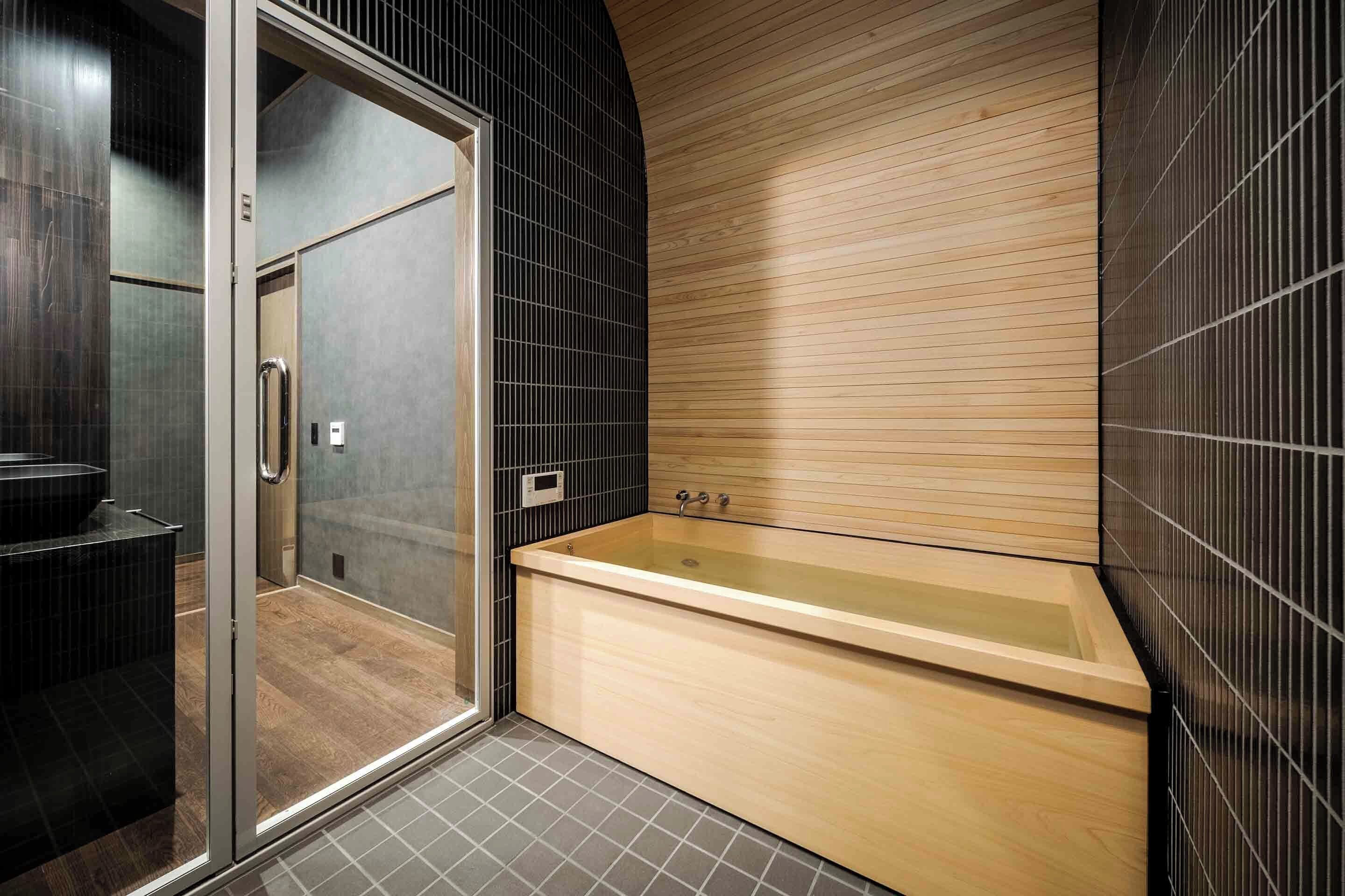 A modern bathroom with a glass shower enclosure, a wooden bathtub, and tiled walls.
