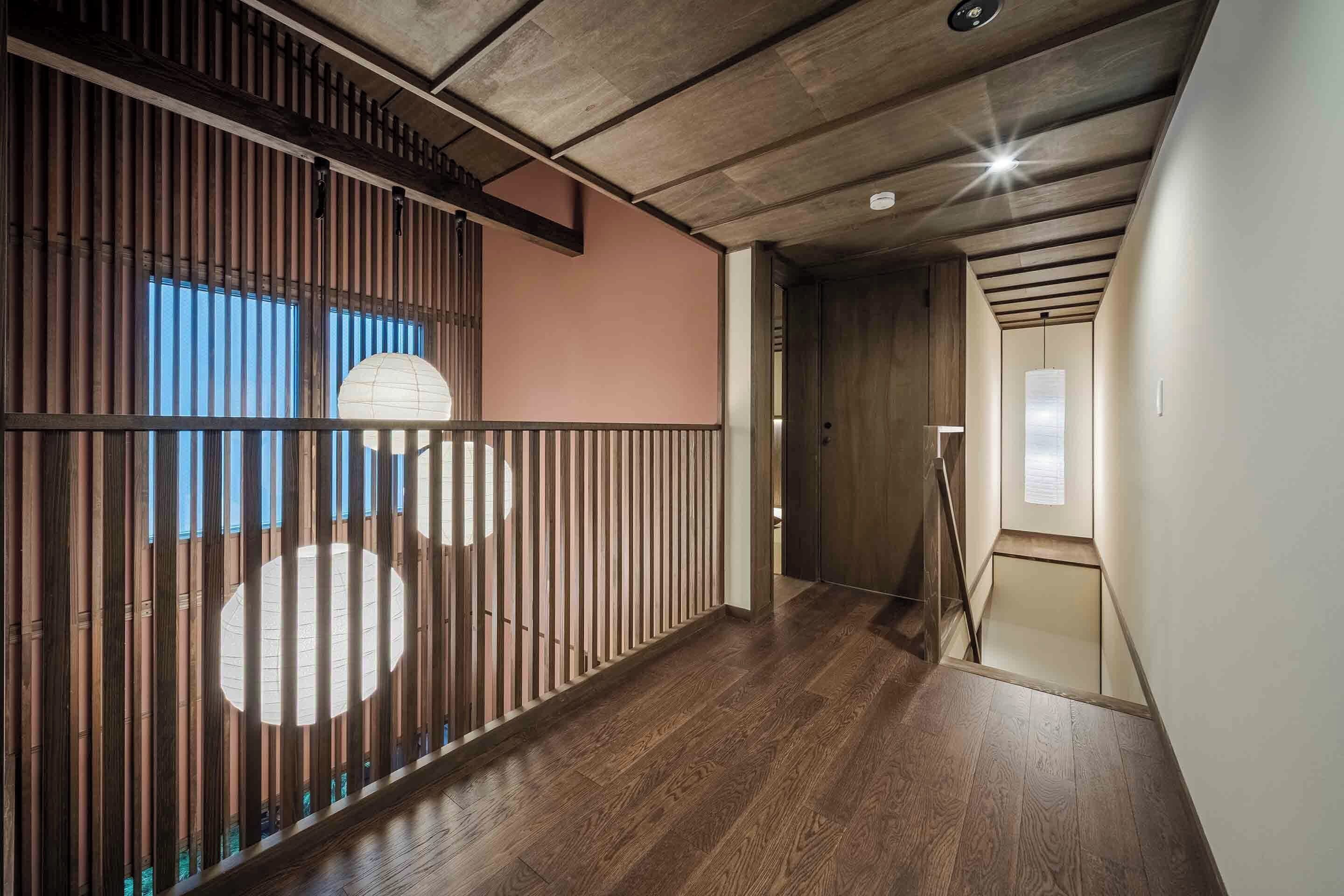 A hallway with wooden flooring, a bamboo partition, and a view of a room with a large window.