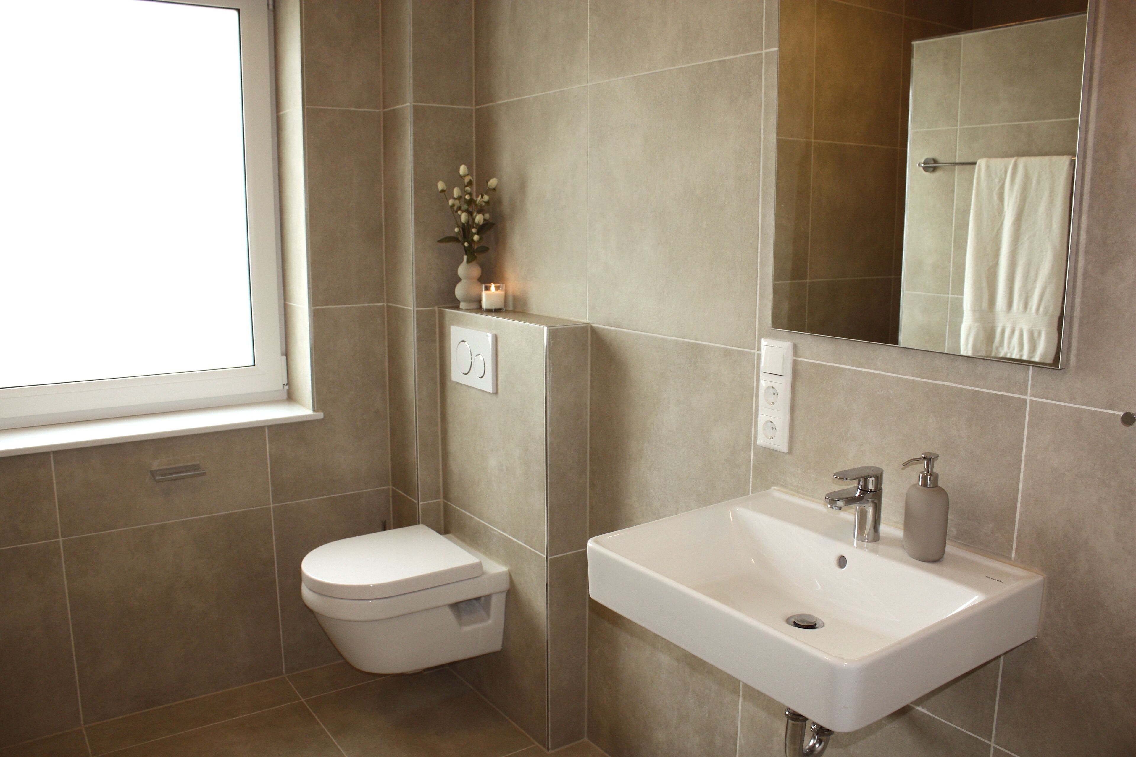 A modern bathroom with a toilet, sink, mirror, and a window.