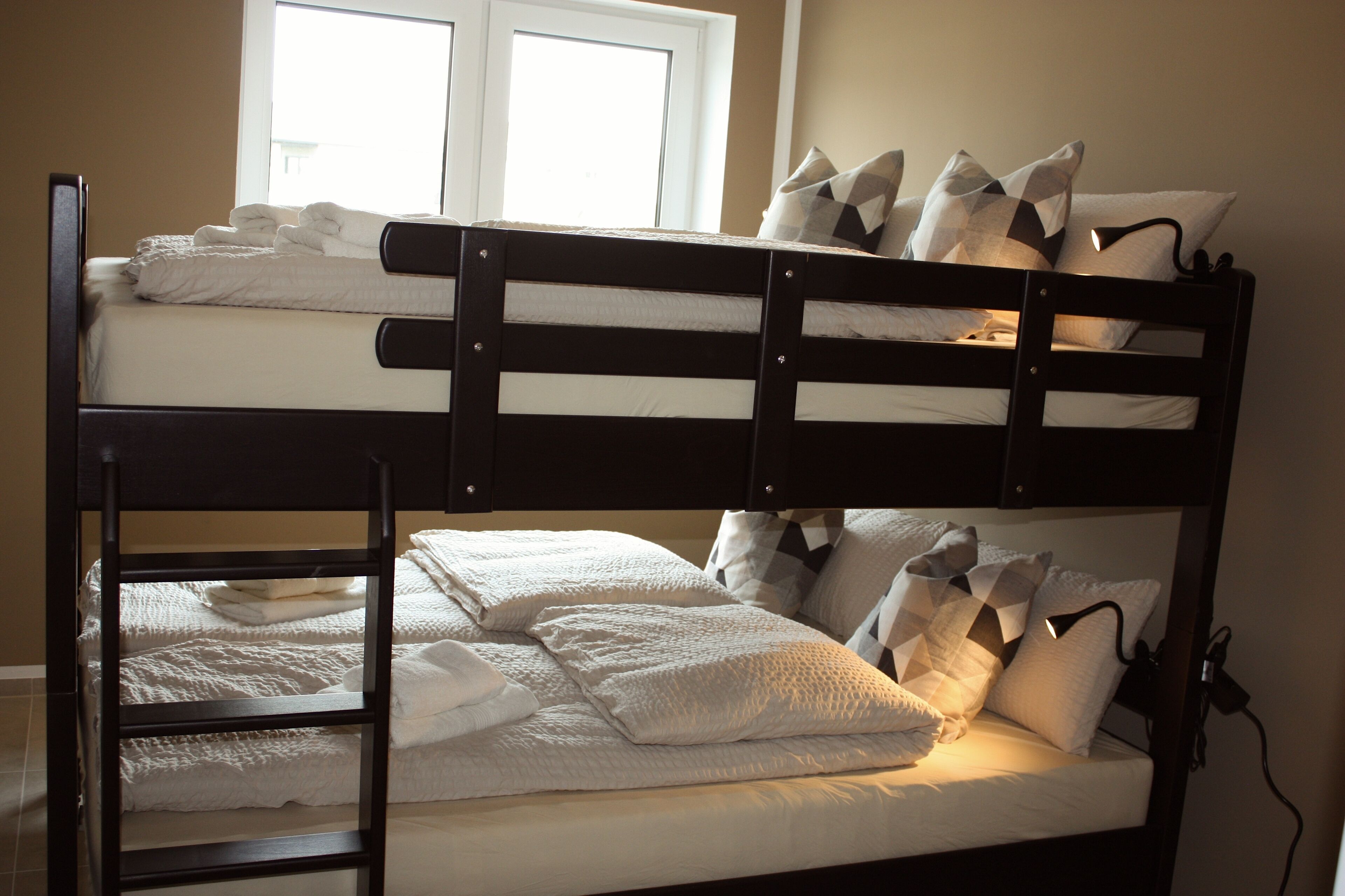 A bunk bed with white bedding and pillows, a ladder, and a window with blinds.