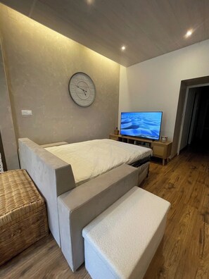 Une chambre à coucher moderne, équipée d’un lit, d’une télévision, d’une horloge et d’une petite table de chevet en bois.